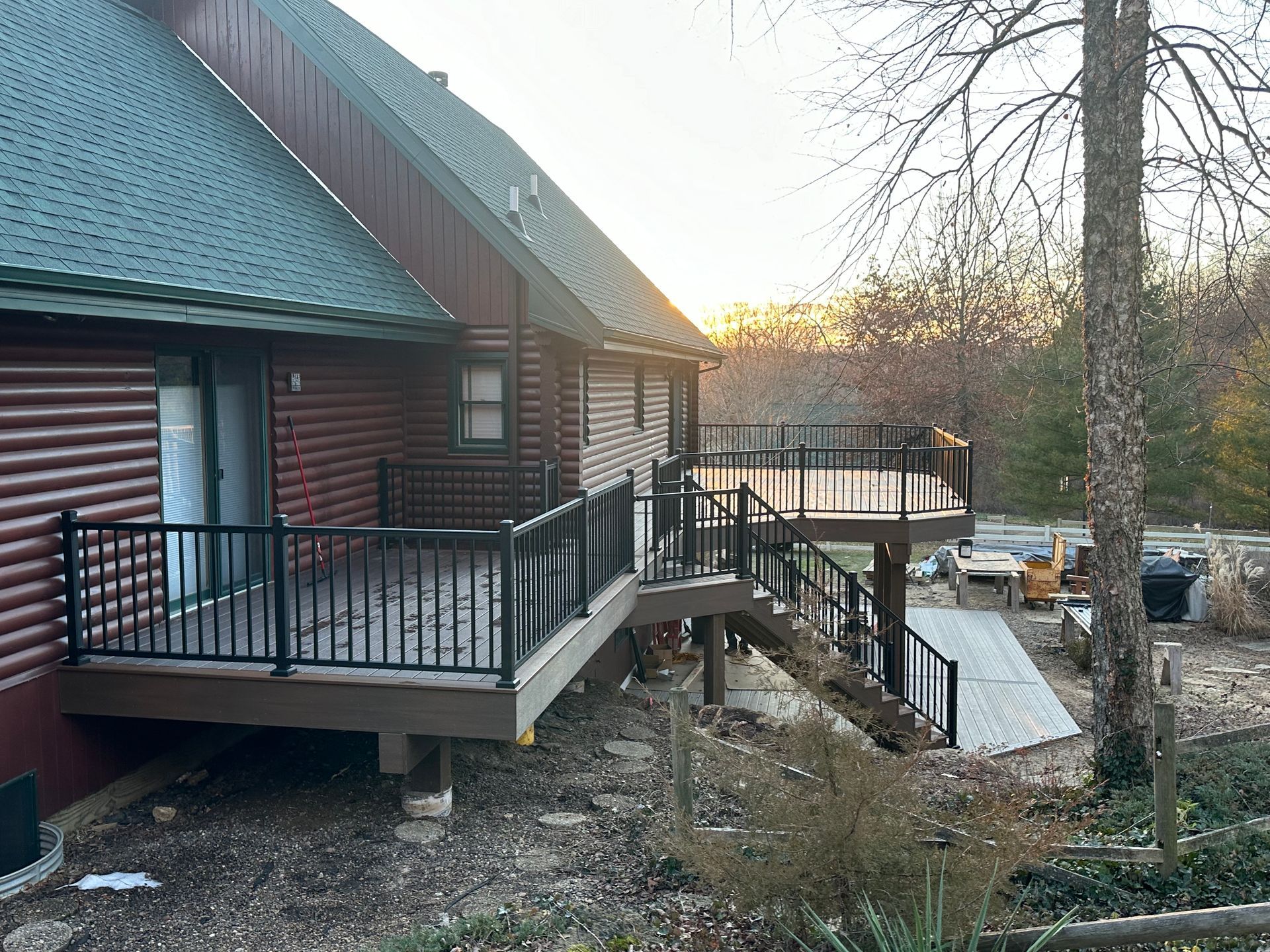 Log cabin deck with black railings overlooking a snowy yard at sunset