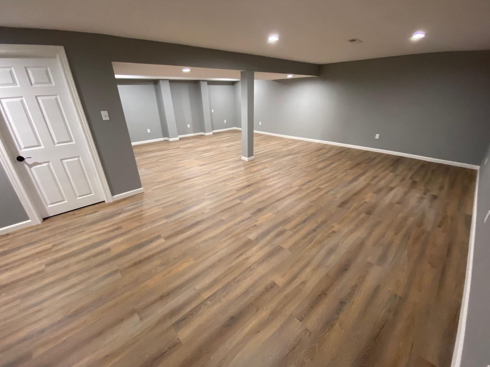 Empty finished basement room with gray walls, wood flooring, and recessed ceiling lights