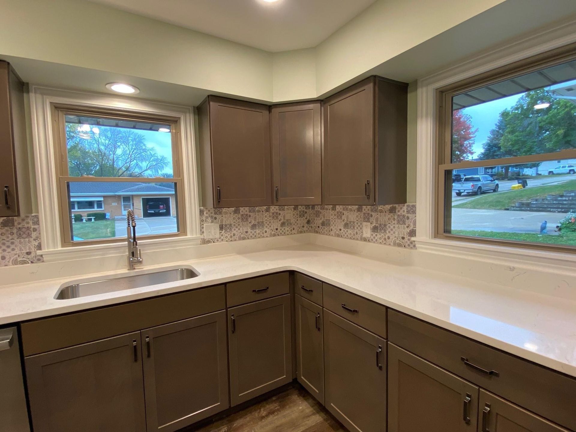 Modern kitchen with brown cabinets, light countertops, tiled backsplash, and two windows over the sink