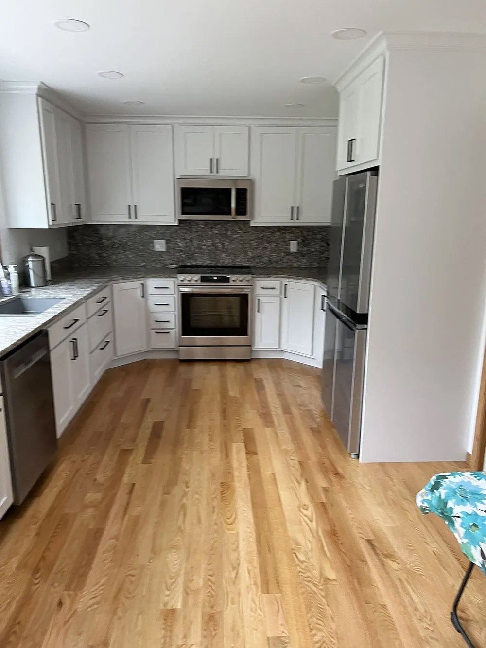 Bright white kitchen with wood floors, stainless appliances, and dark tile backsplash
