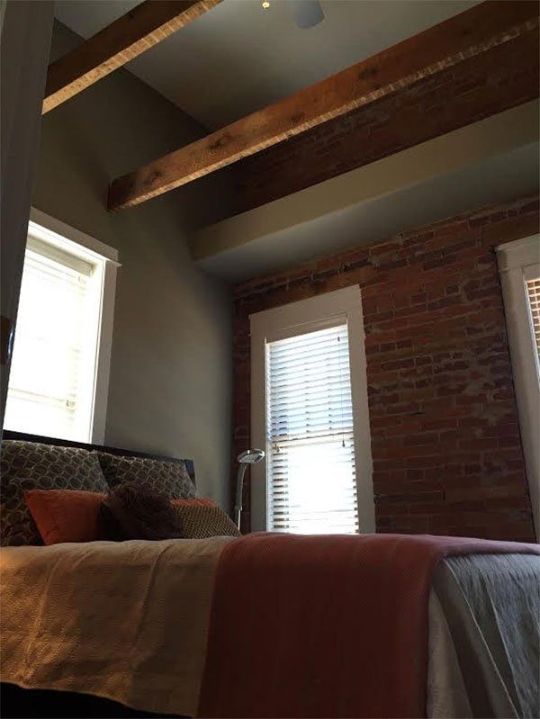 Cozy bedroom with exposed brick, wooden beams, and a bed by sunlit windows