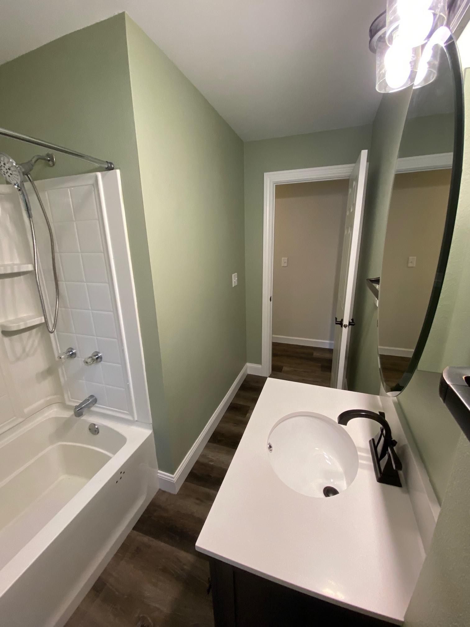 Small bathroom with green walls, white vanity, tub, and mirror facing a doorway.