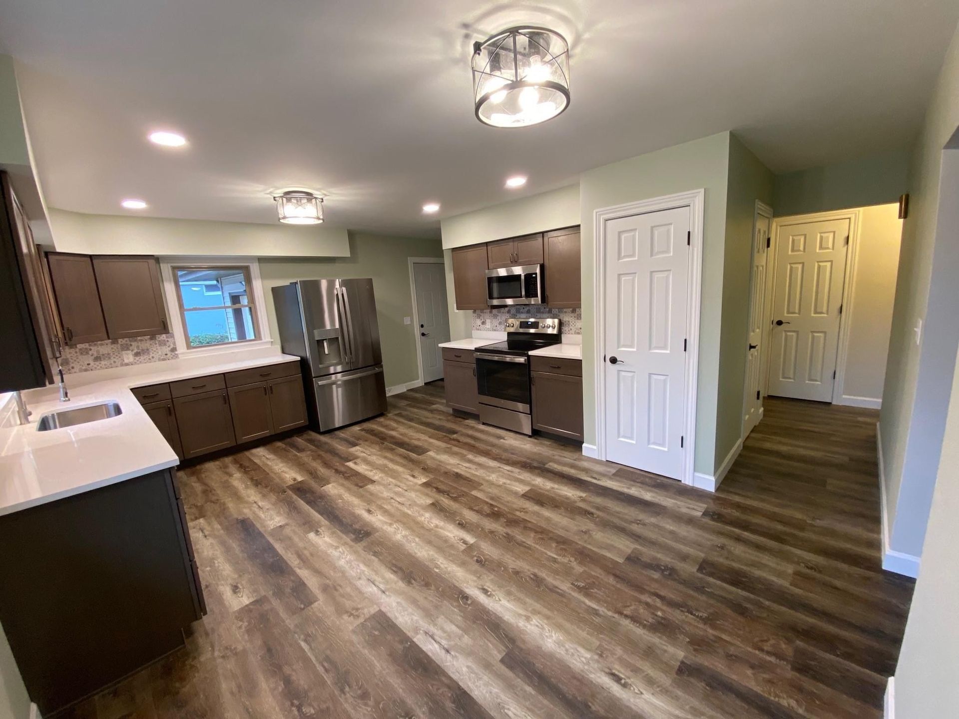 Spacious modern kitchen with stainless steel appliances, dark cabinets, and wood-look flooring.