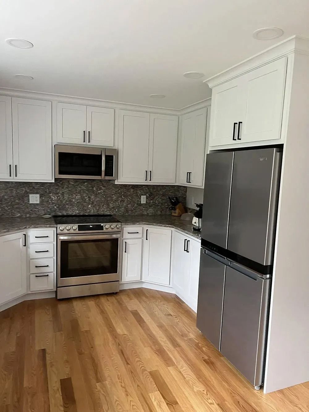 Bright kitchen with stainless steel appliances, white cabinets, and wood floors