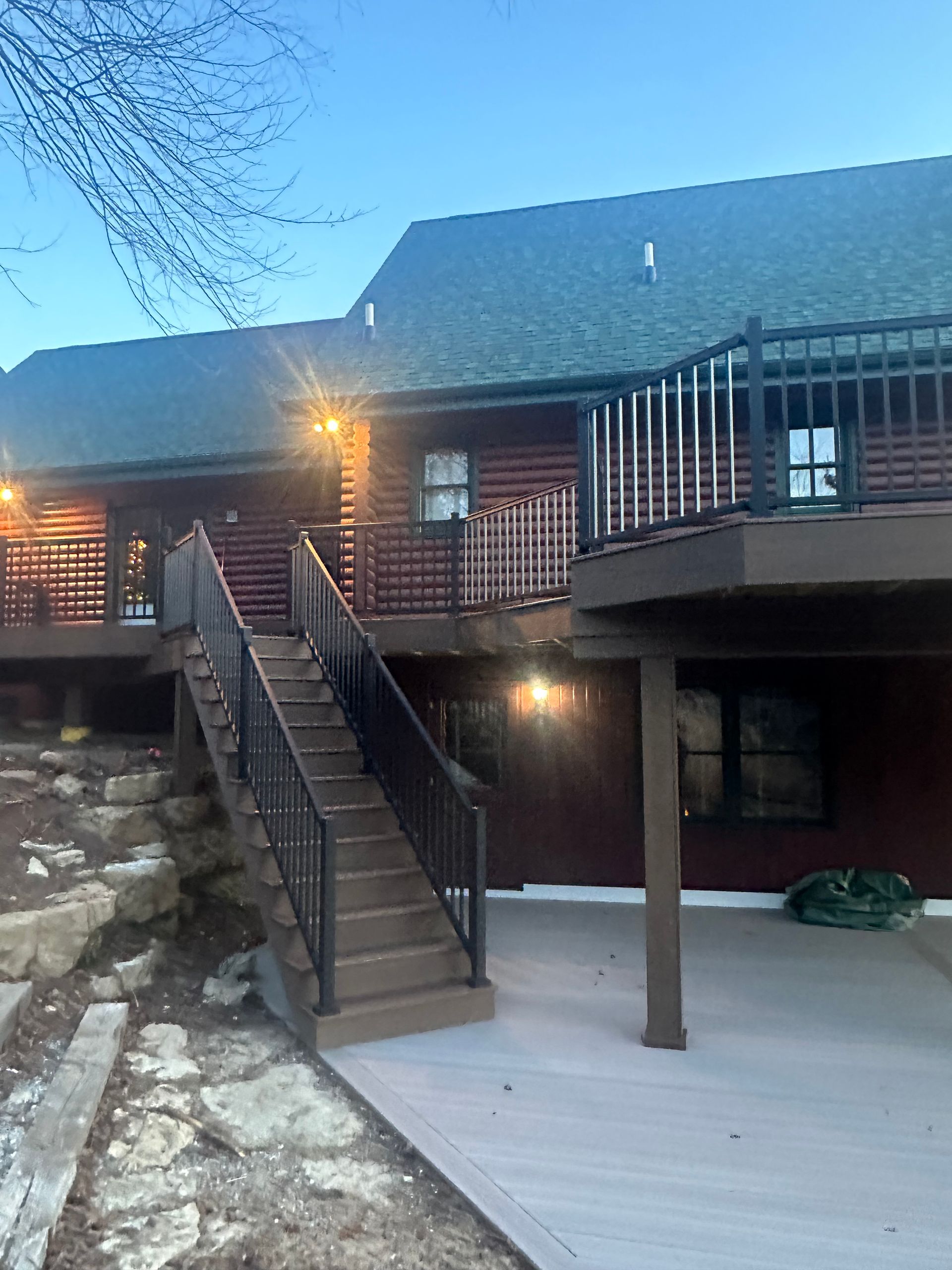 Log cabin deck with stairs, black railings, and a snow-covered patio at dusk
