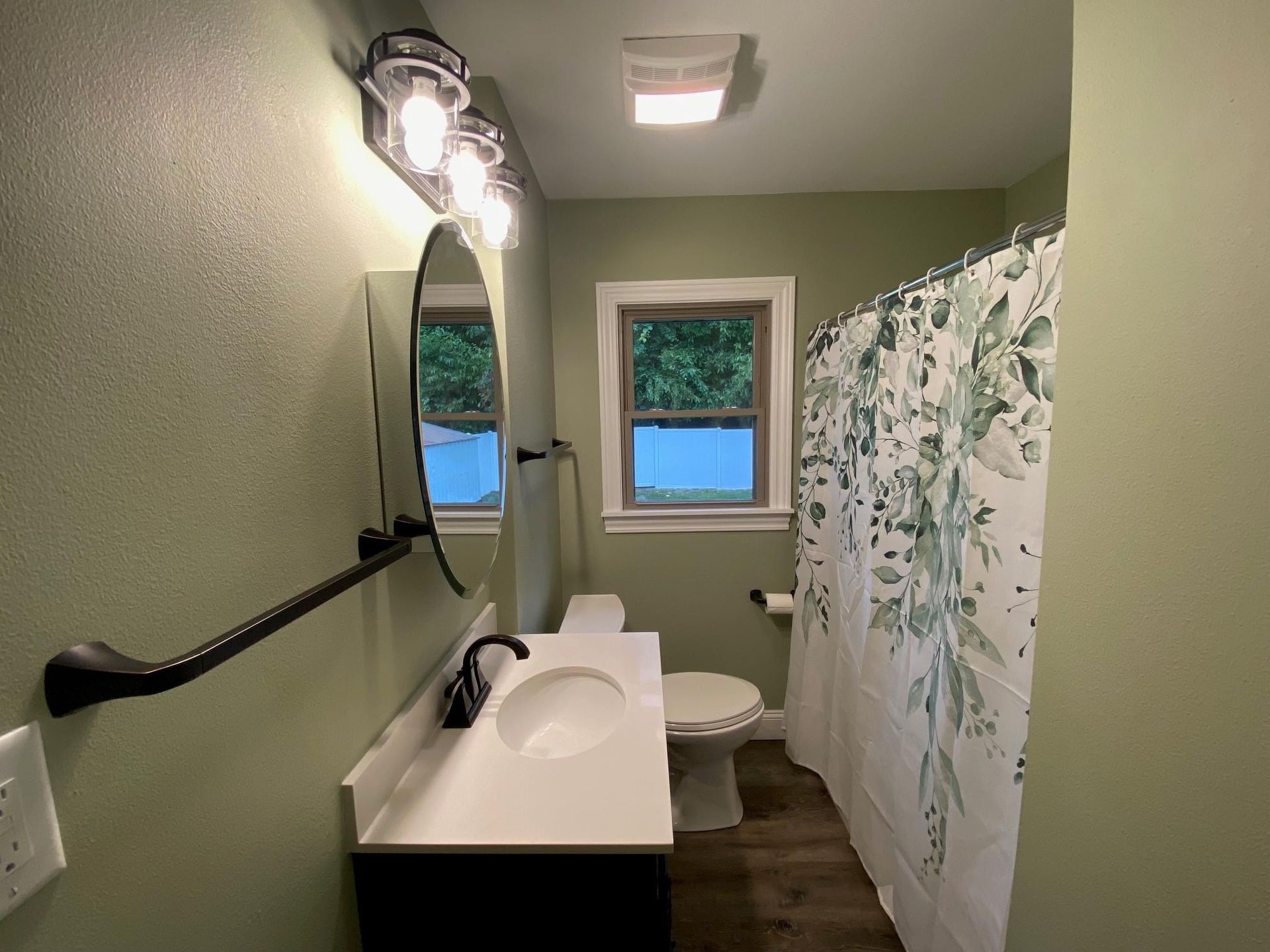 Small bathroom with white sink, toilet, shower curtain, mirror, and green walls.