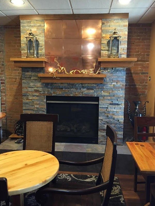 Restaurant fireplace with stone surround, wooden mantel, and tables and chairs in the foreground