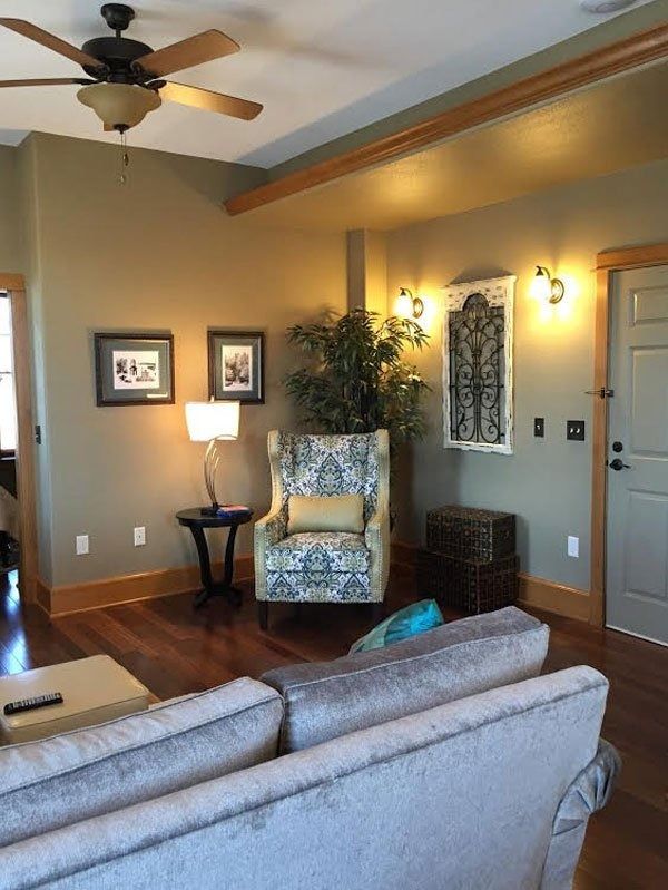 Cozy living room with gray sofa, patterned armchair, wall art, lamps, and ceiling fan
