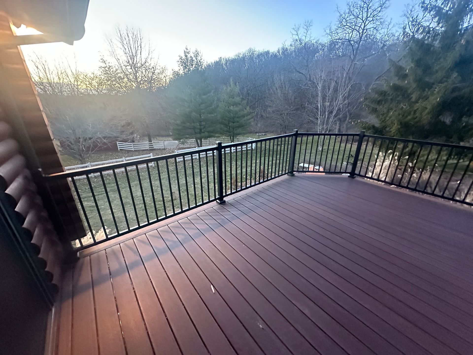 Wooden deck with black railing overlooking a wooded yard at sunset