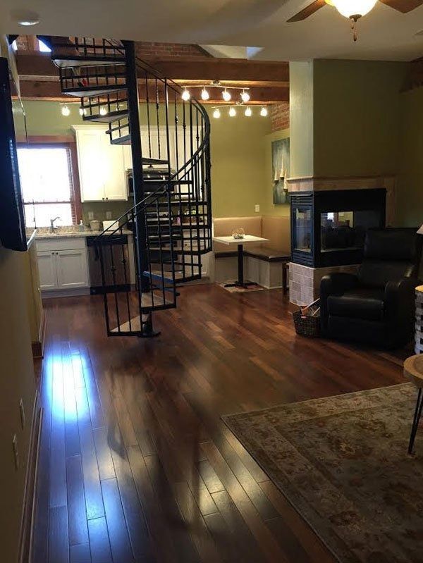 Living room with spiral staircase, hardwood floors, black leather chair, and kitchen area in the background