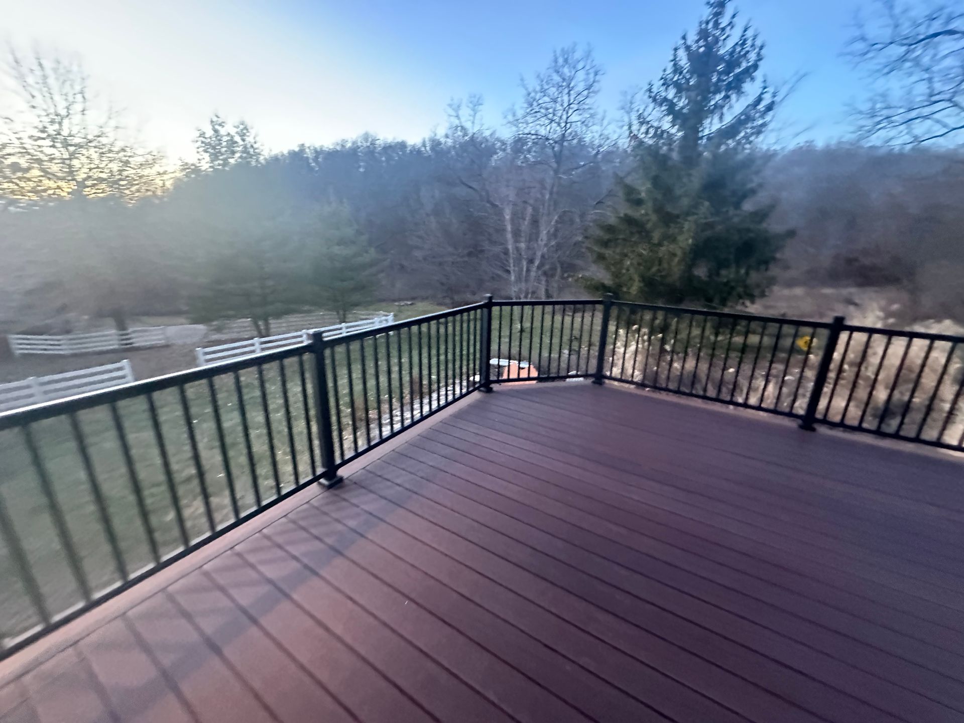 Empty wooden deck with black railing overlooking a wooded landscape at dusk