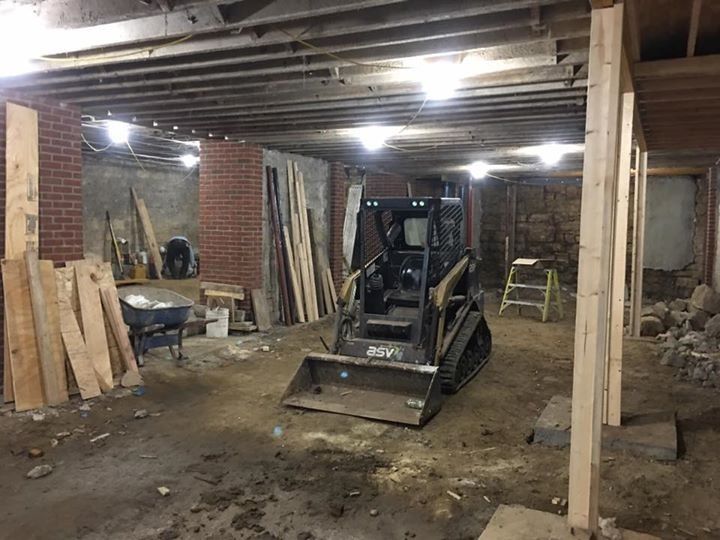 Construction equipment in a dim unfinished basement with exposed beams and brick walls