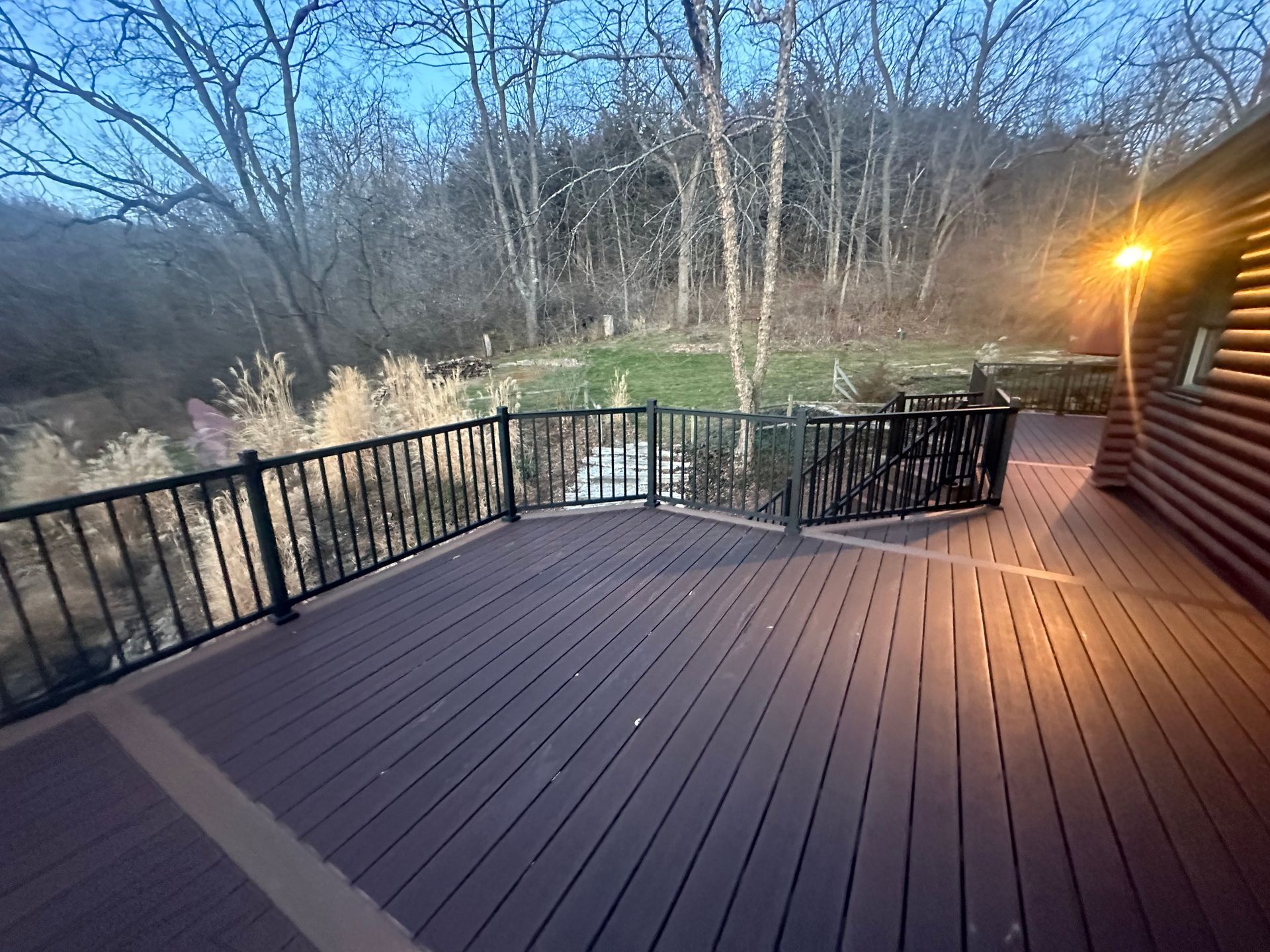 Wooden deck with black railing beside a cabin, overlooking a wooded valley at dusk
