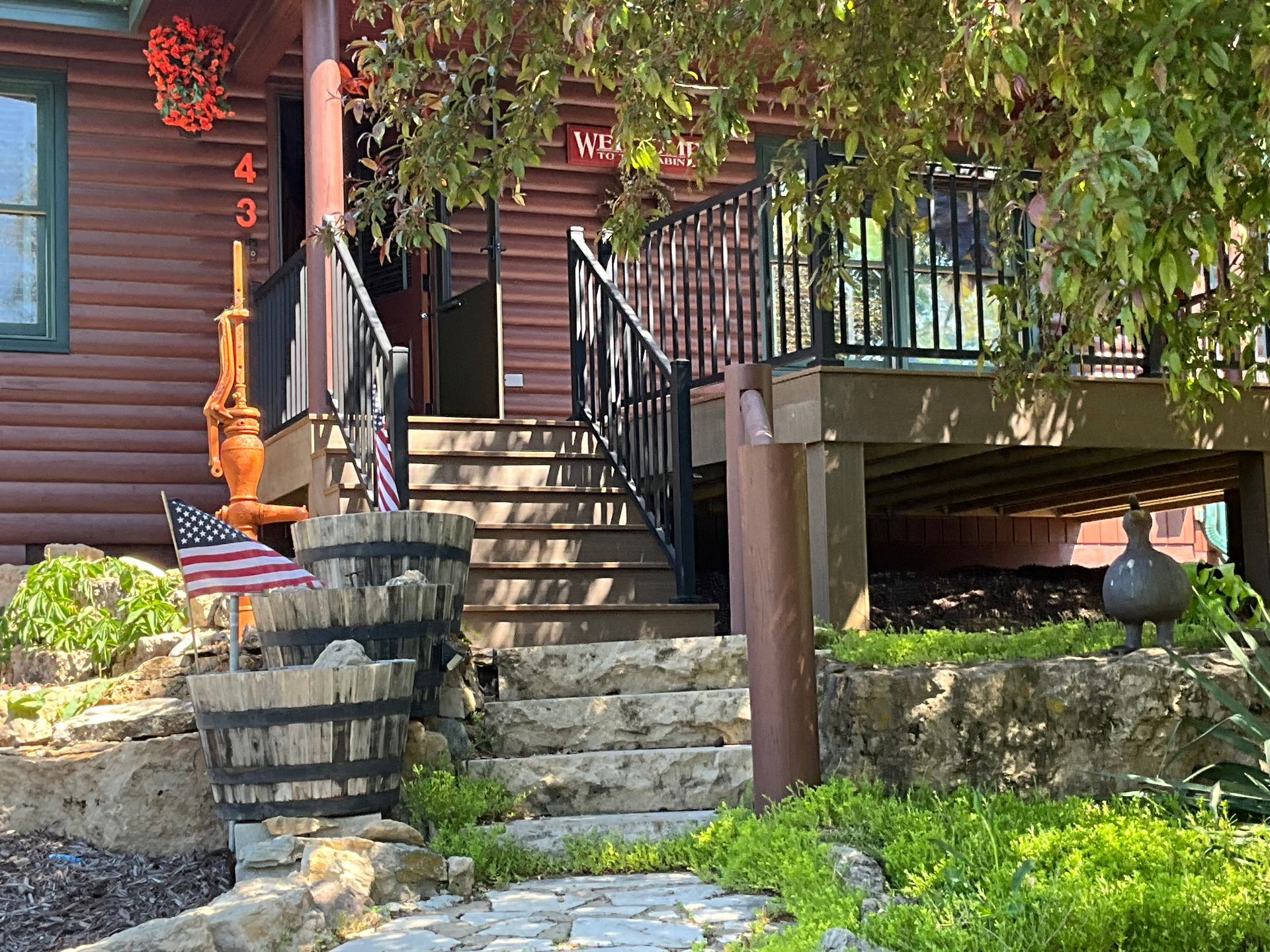 Stone steps lead to a rustic house entrance with black railings, barrel decor, and a small bridge above the yard