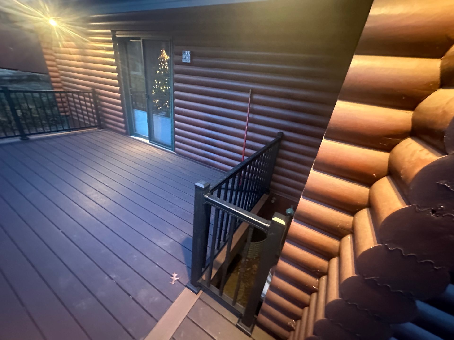 Wooden cabin deck with black railing, blue door, and sunlit log wall at sunset