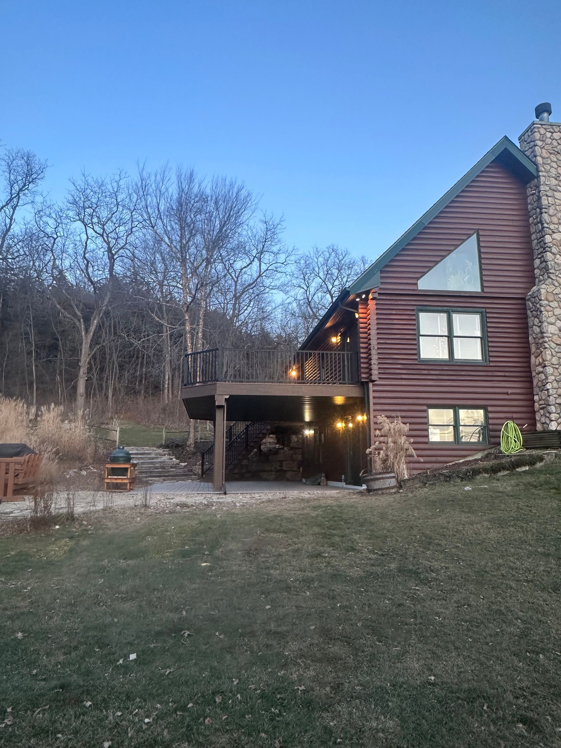 Rustic house with a covered porch at dusk, set beside a grassy yard and leafless trees.