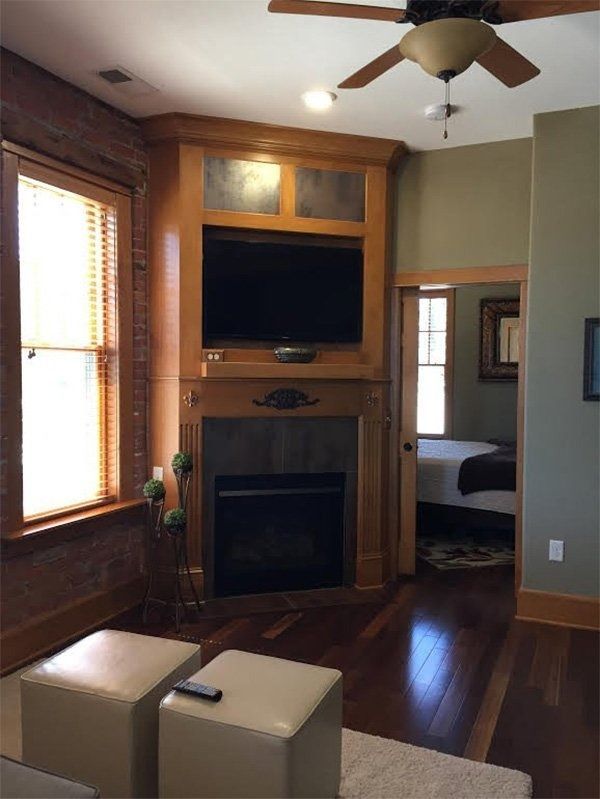 Cozy living room with a fireplace, wall-mounted TV, hardwood floors, and a ceiling fan.