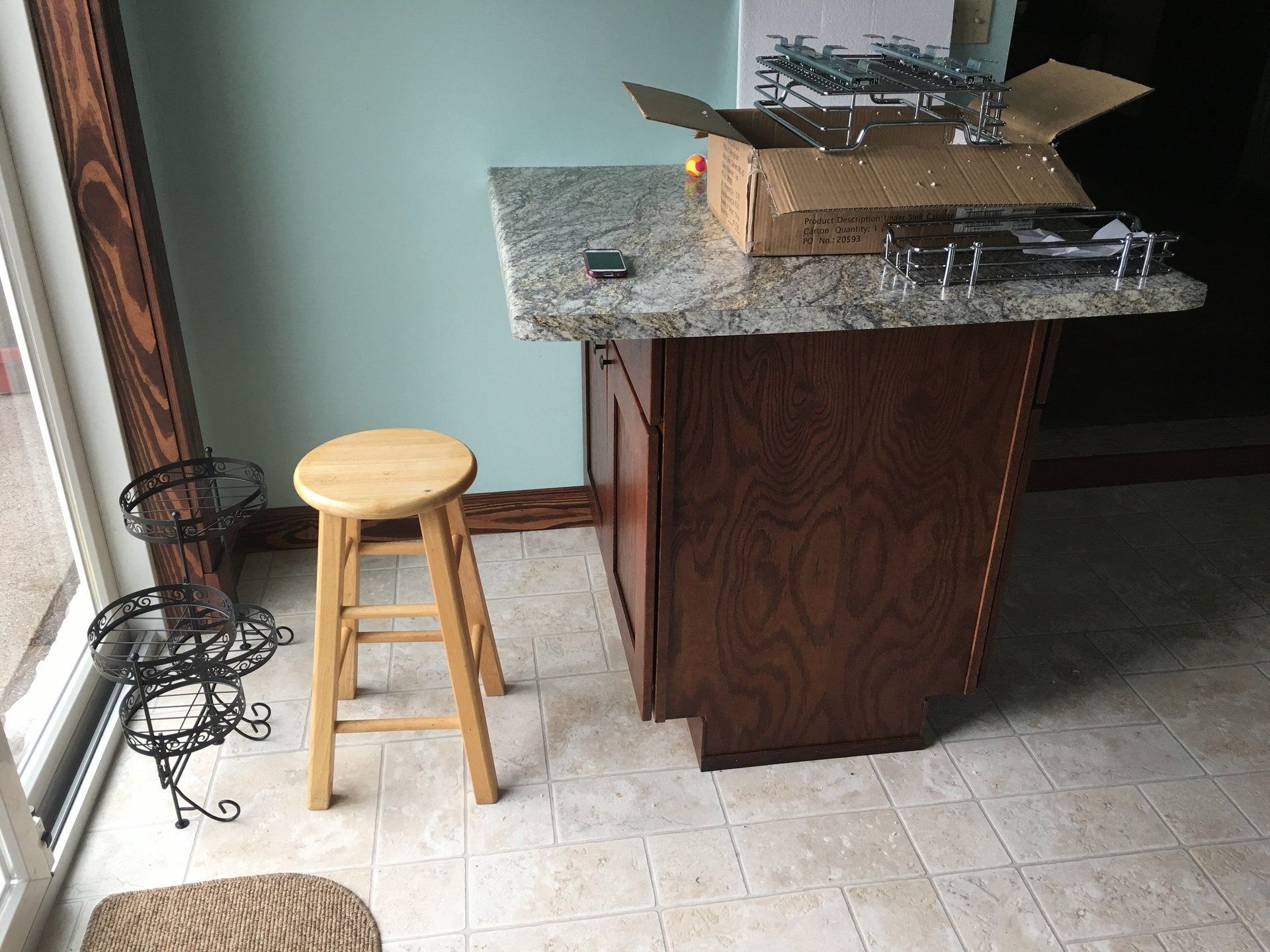 Kitchen island with open cardboard boxes, a wooden stool, and a metal wire stand on a tiled floor.