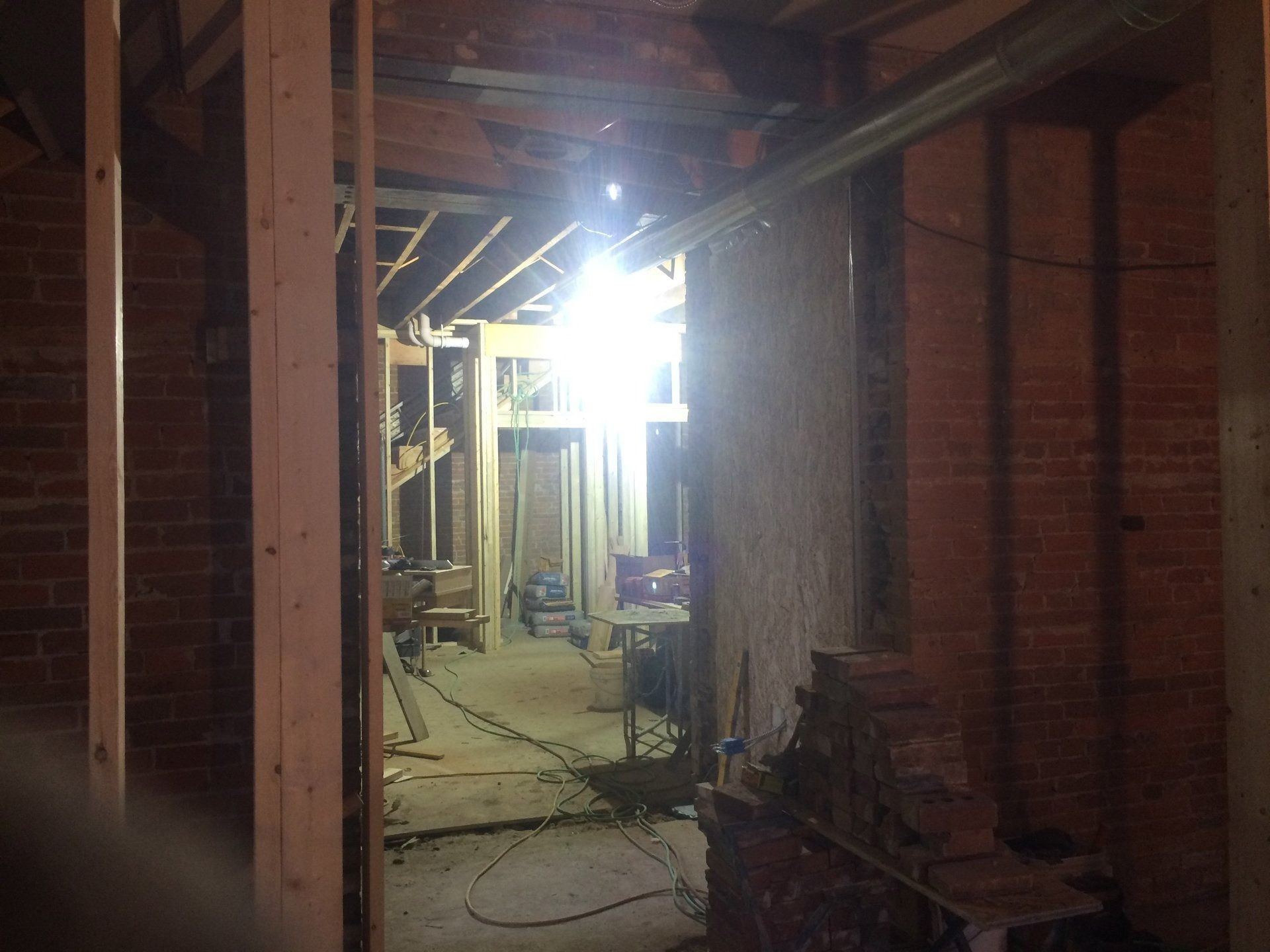 Dim construction hallway with brick walls, exposed framing, cables, and bright light at the far end.