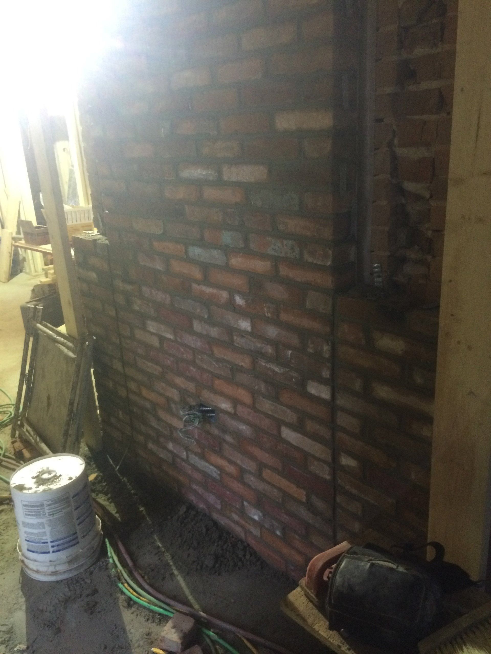 Brick wall in a construction area with a bucket, cables, and tools on the floor.
