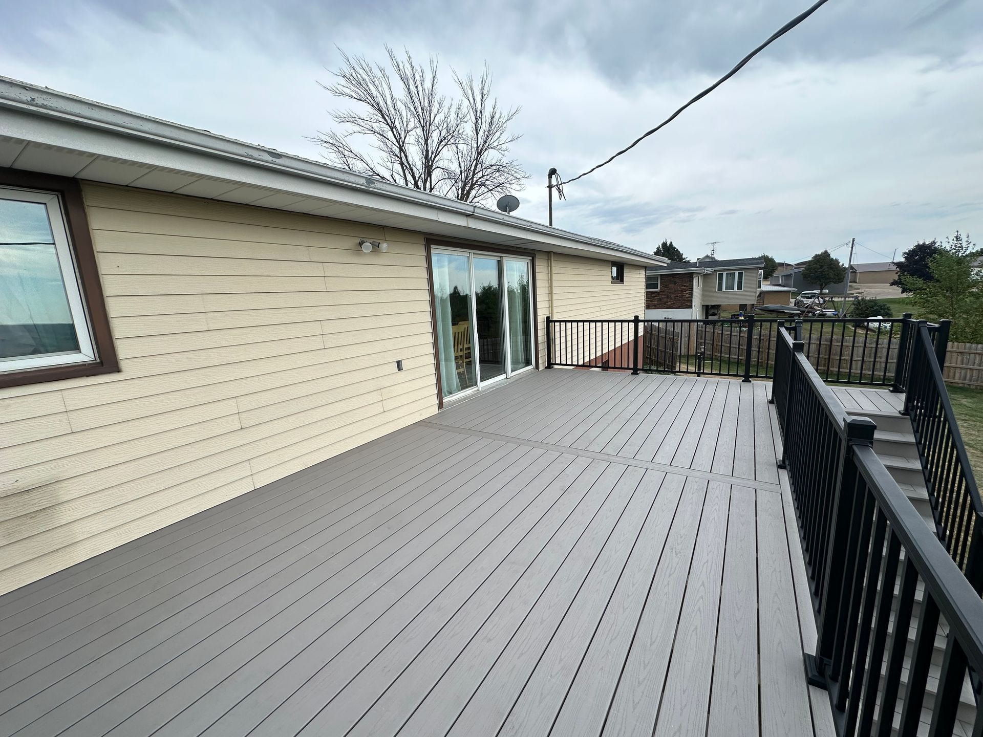 Spacious gray deck beside a beige house, with black railings and sliding glass doors.
