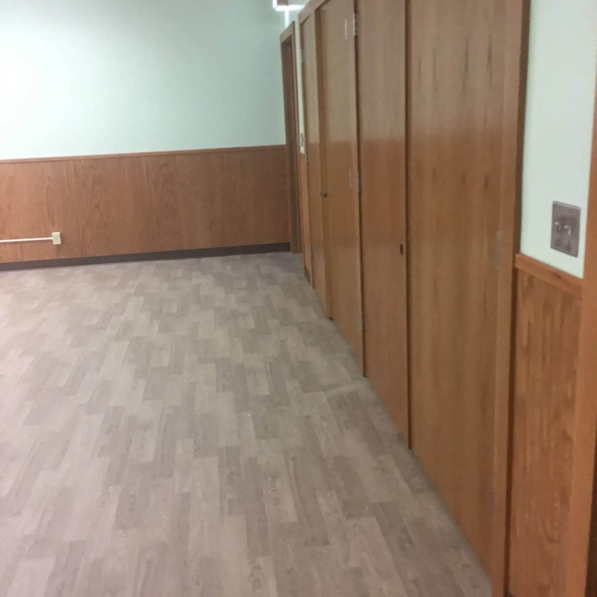 Empty hallway with wood-paneled walls, carpeted floor, and closed closet doors.