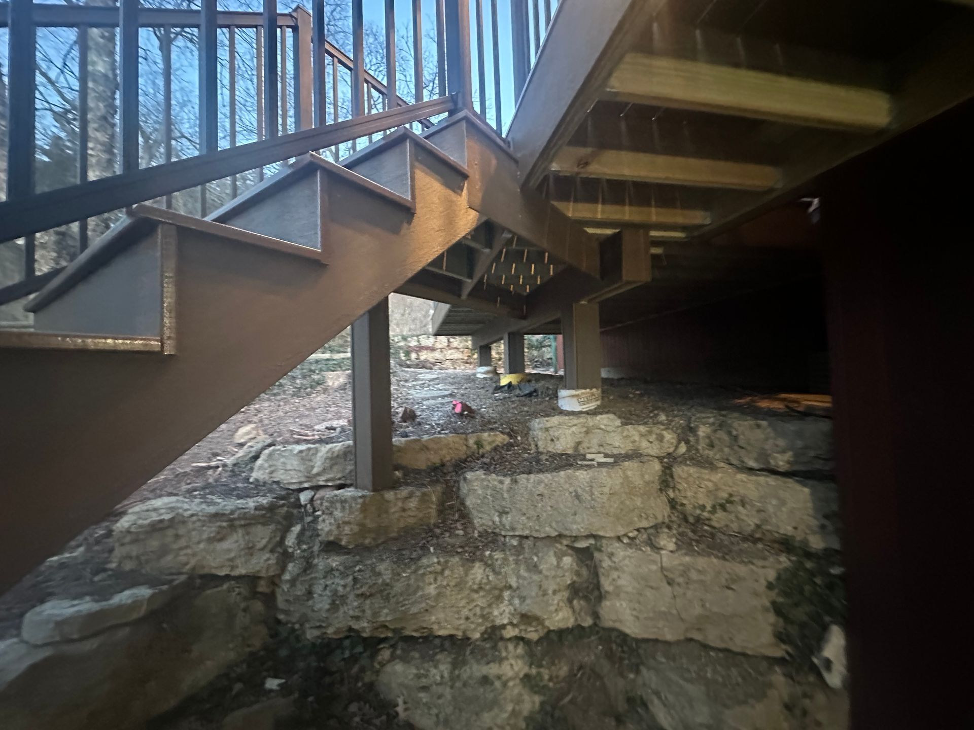 Underside of a wooden footbridge over a rocky stream in a wooded area