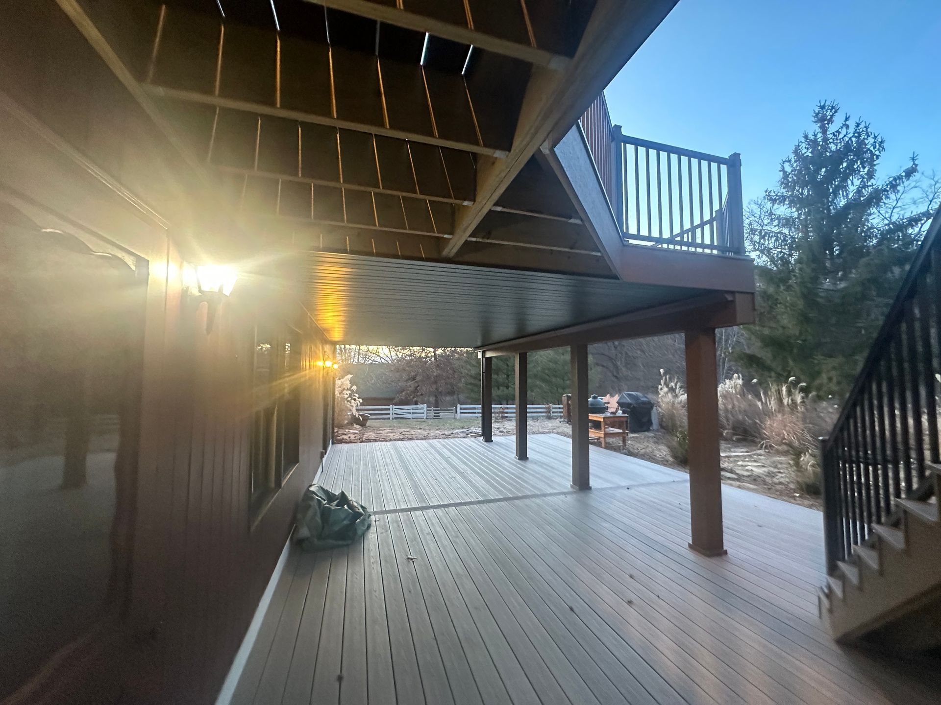 Covered wooden deck with staircase, railing, and sunset light streaming in from the left.