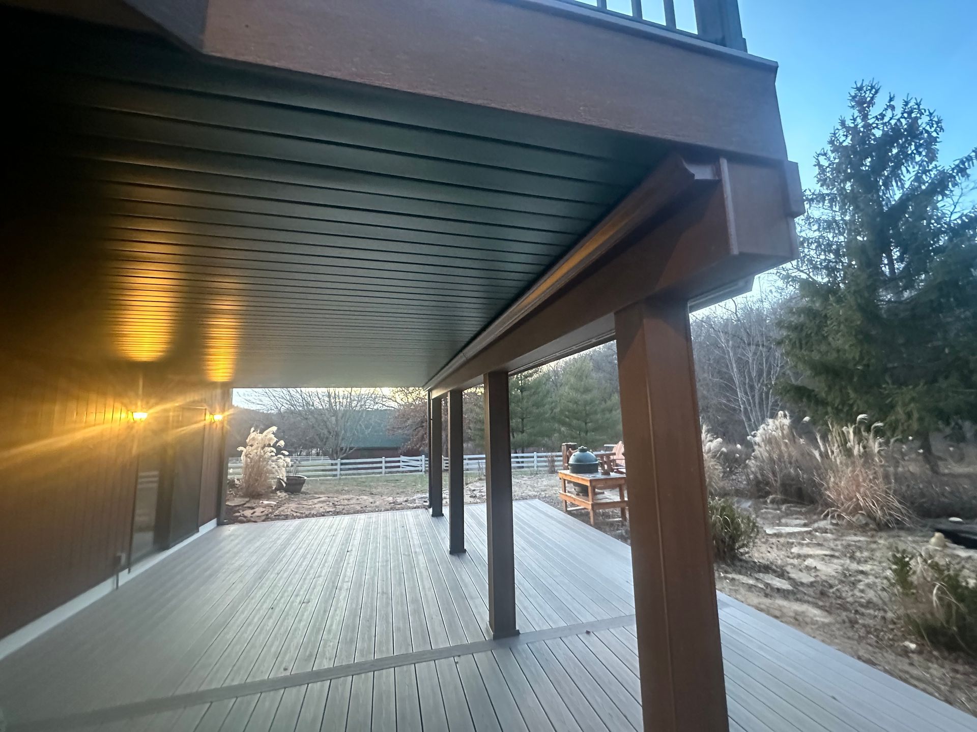 Covered wooden deck with a view of a snowy yard and trees at dusk