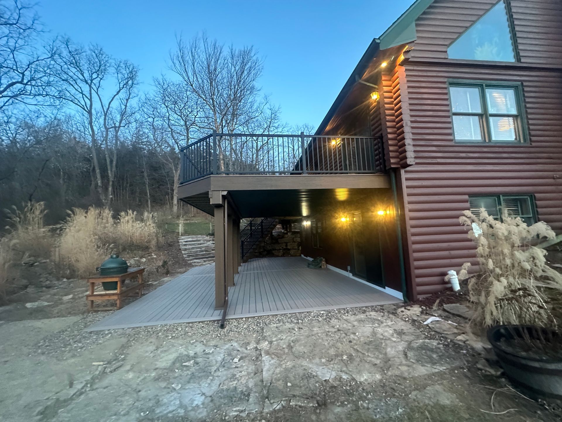 House with carport and balcony at dusk, with warm lights and bare trees in the yard