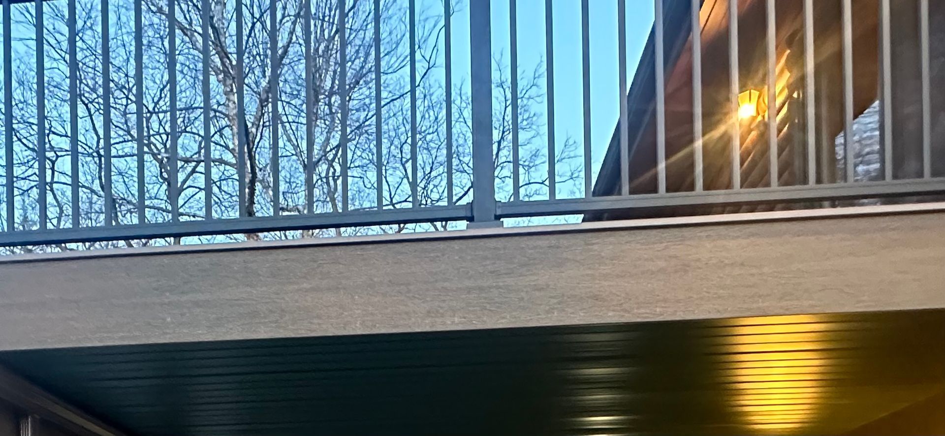 Snow-covered railing beside a lit building at dusk, seen from a lower angle