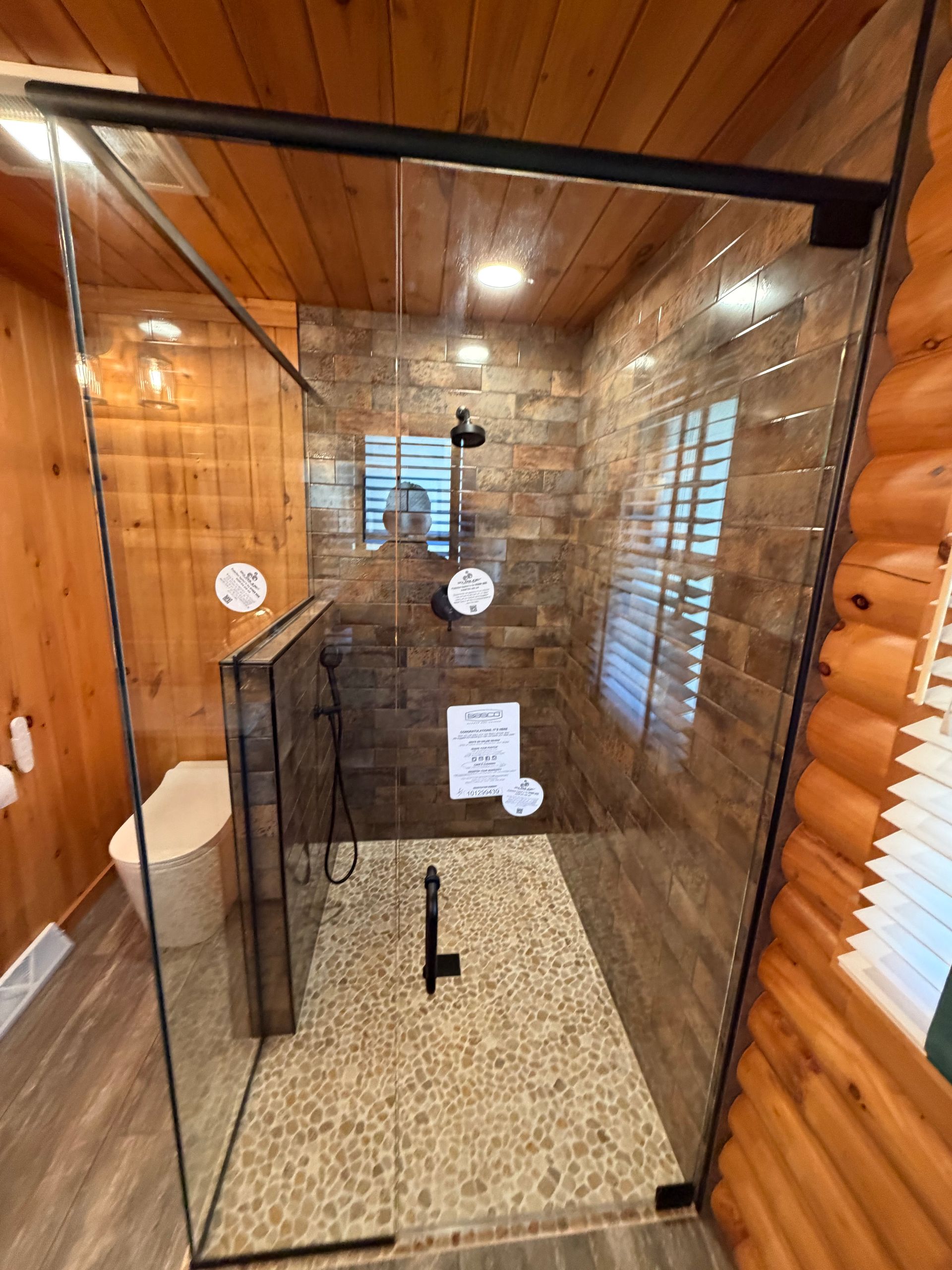 Glass-enclosed shower with black trim in a wood-paneled bathroom with beige tile floor