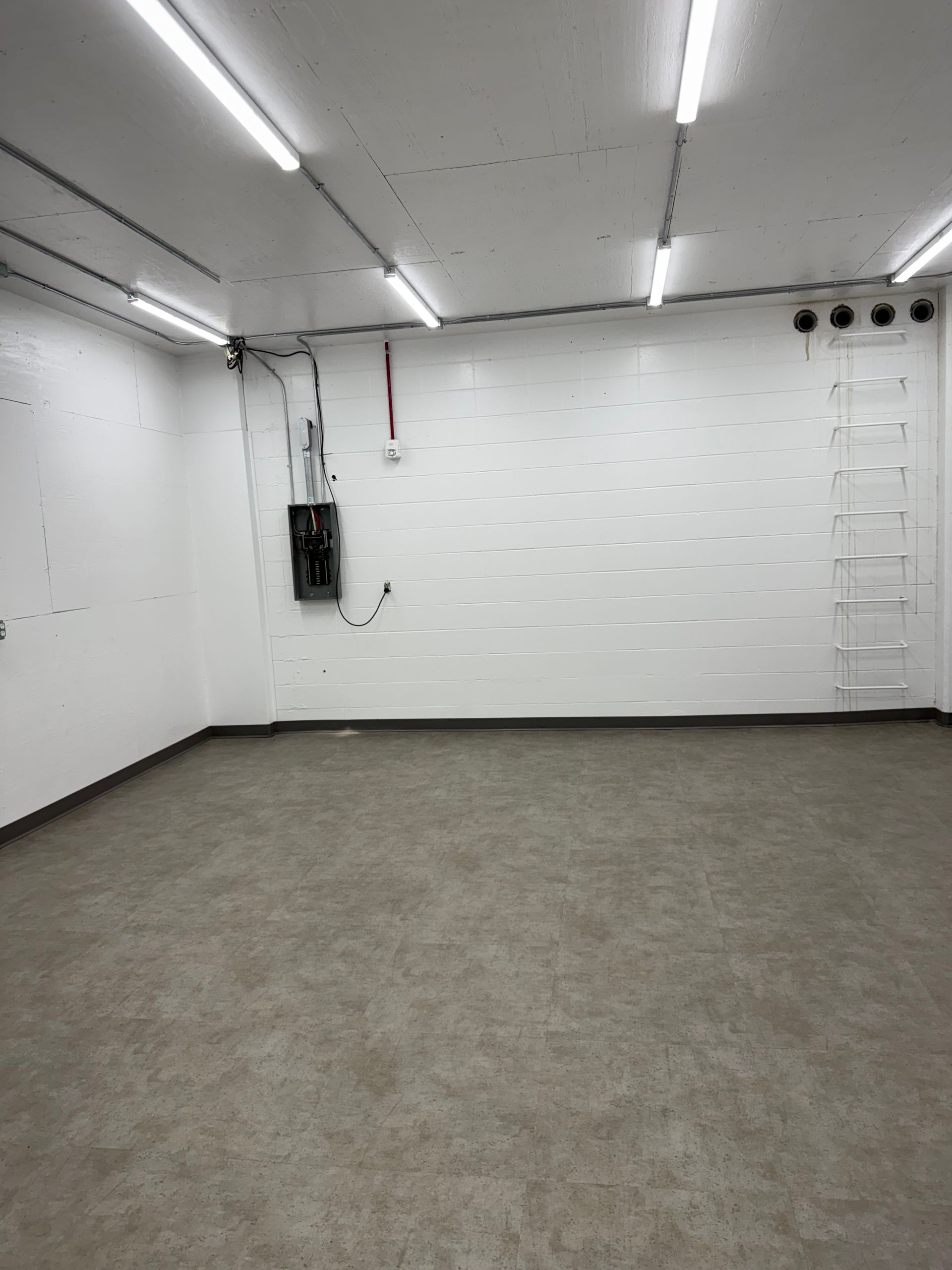 Empty white room with gray carpet, fluorescent lights, and wall-mounted equipment