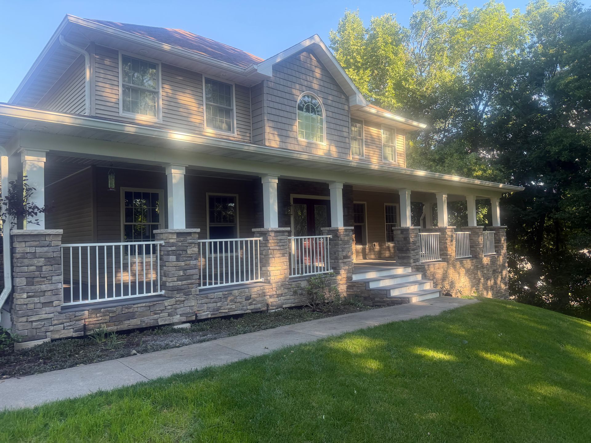 Stone house with a front porch, white railings, and green lawn in daylight
