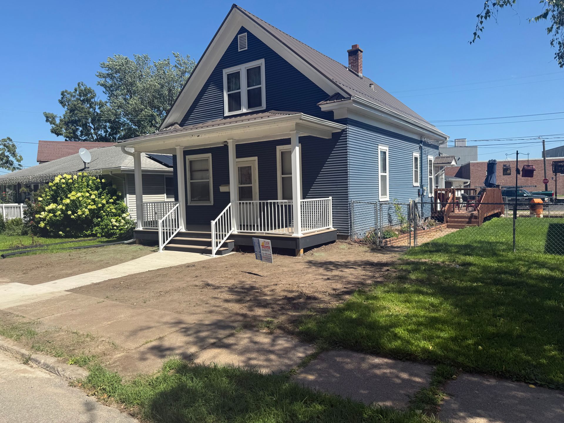 Small blue house with white trim and a front porch on a sunny residential street