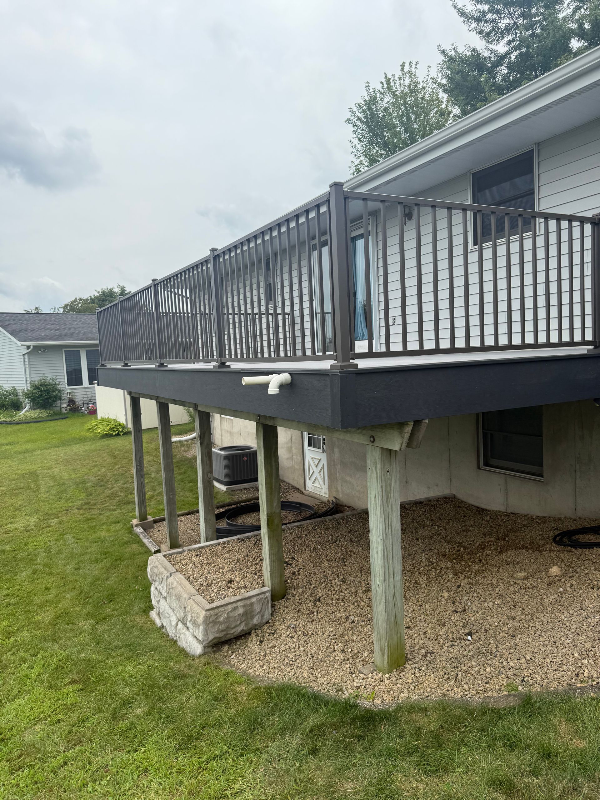 Elevated backyard deck with black railing, gravel underneath, and concrete support posts beside a house