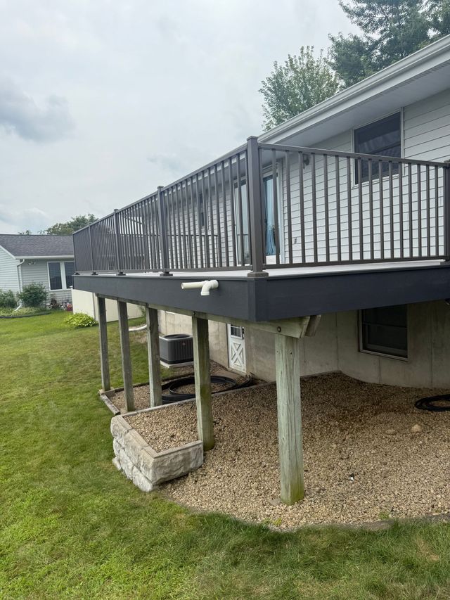 Raised backyard deck with black railing on concrete posts over a grassy yard and gravel below