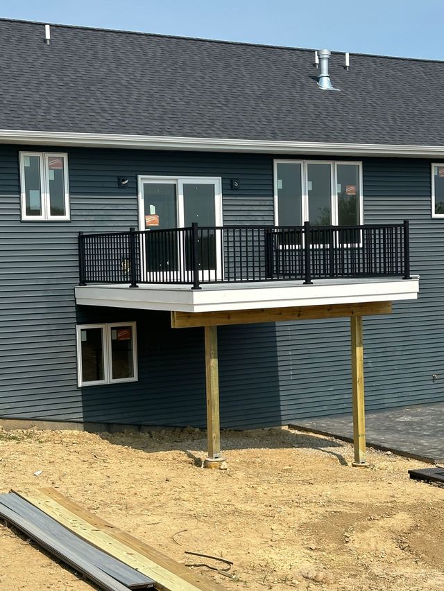 Raised deck with black railing on a gray house above a dirt yard.