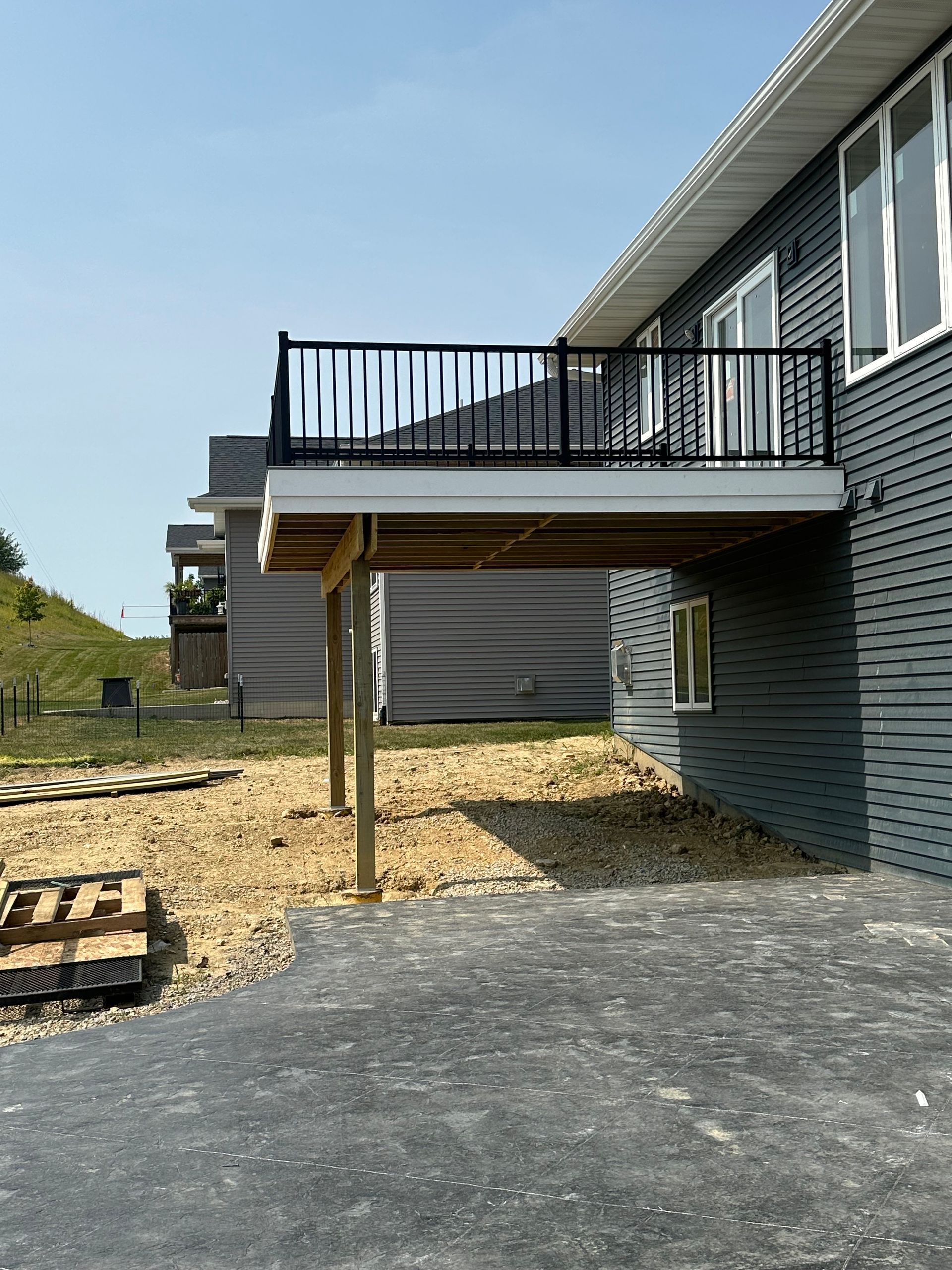 House exterior with raised deck, black railing, and gravel yard under a clear sky