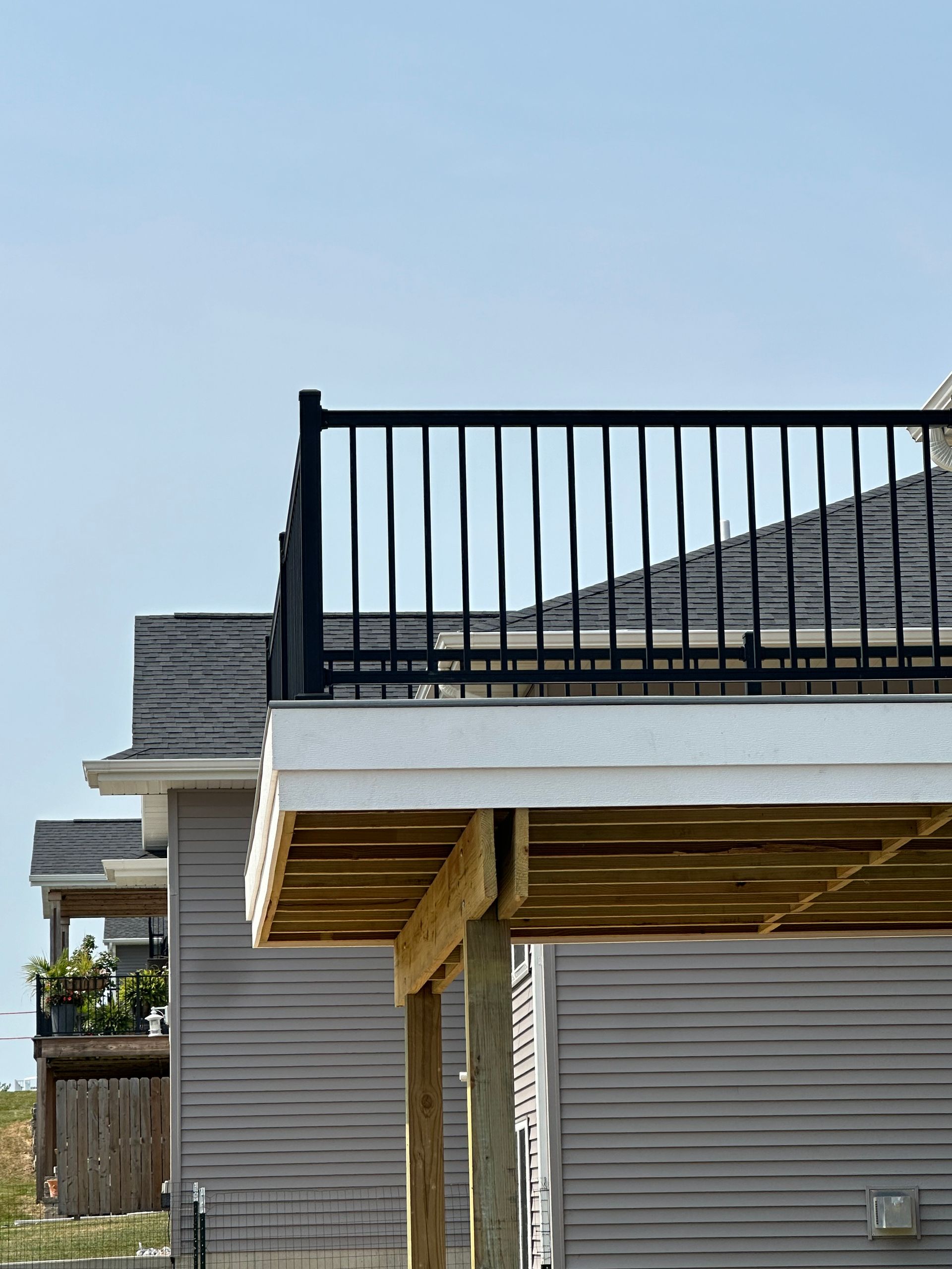 Raised deck with black railing and gray house siding under a clear blue sky