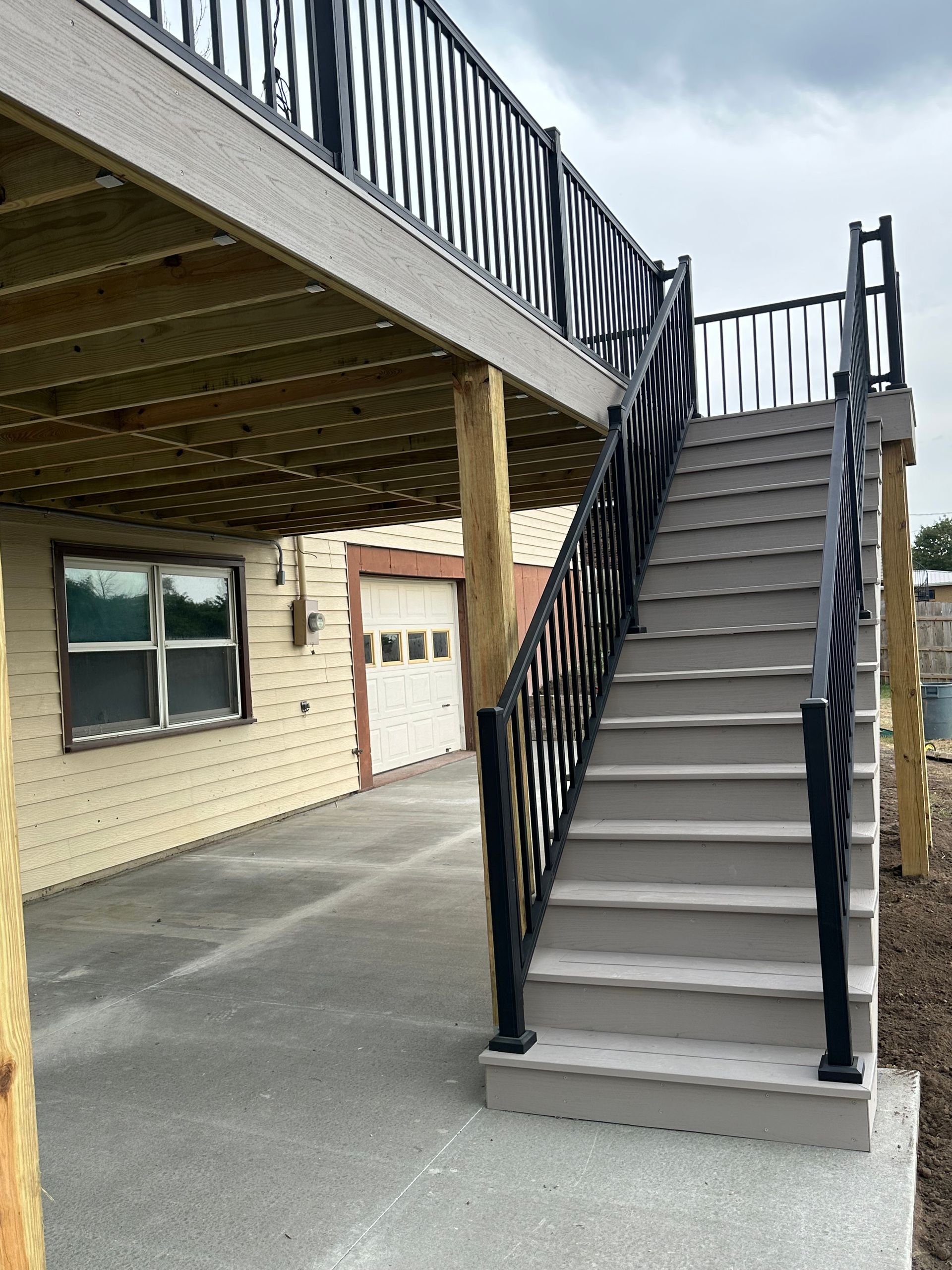 Covered outdoor staircase with black railings leading to an upper deck beside a brick building.