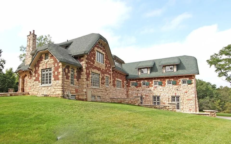 Stone house with red trim and dormer windows on a grassy hill under a bright sky