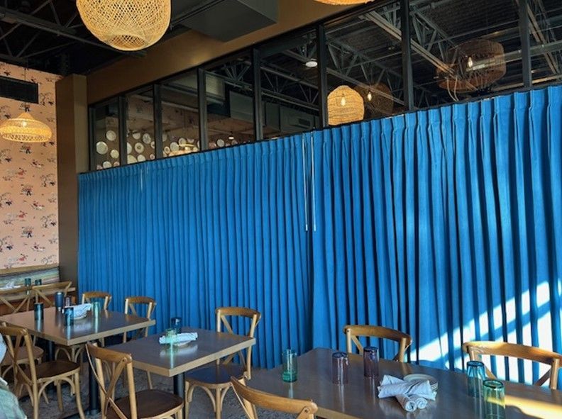 A restaurant with blue curtains and tables and chairs.
