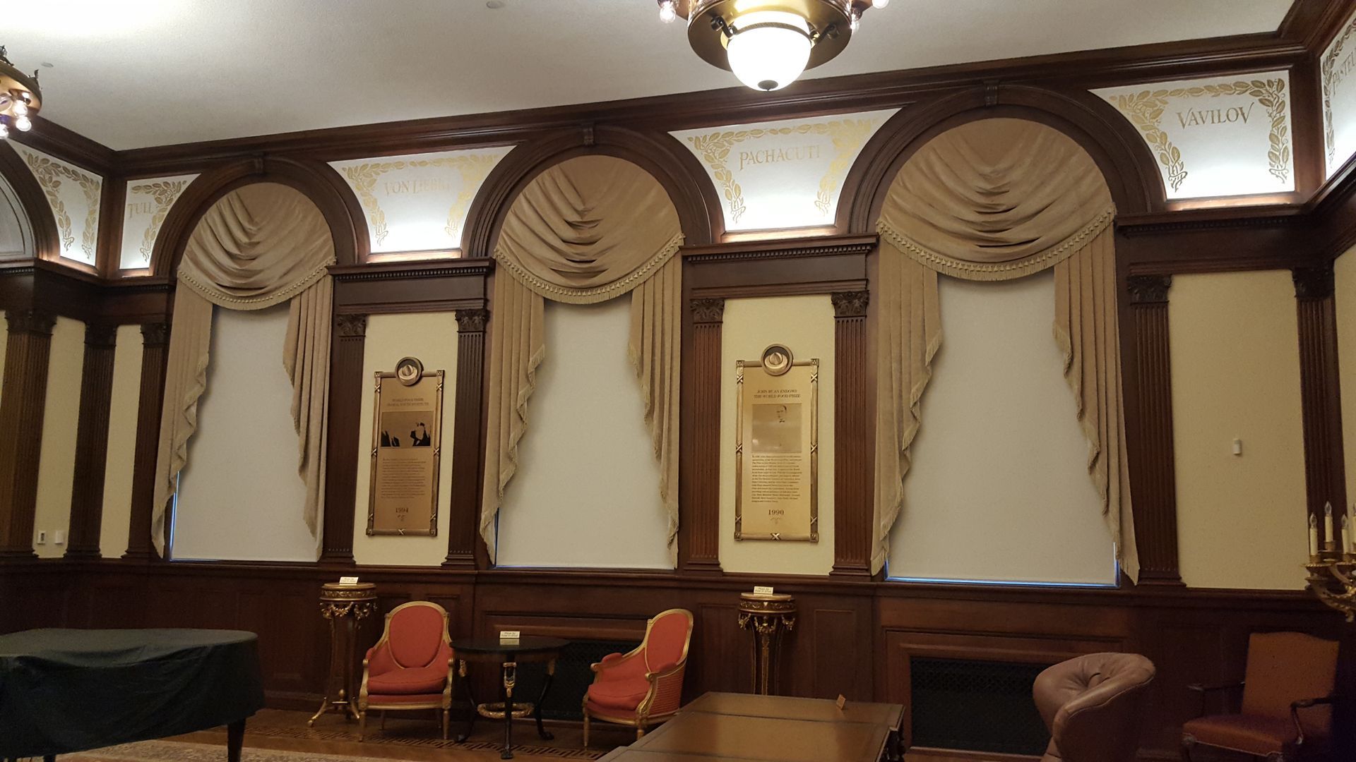 A room with a piano , chairs , curtains and a fireplace.