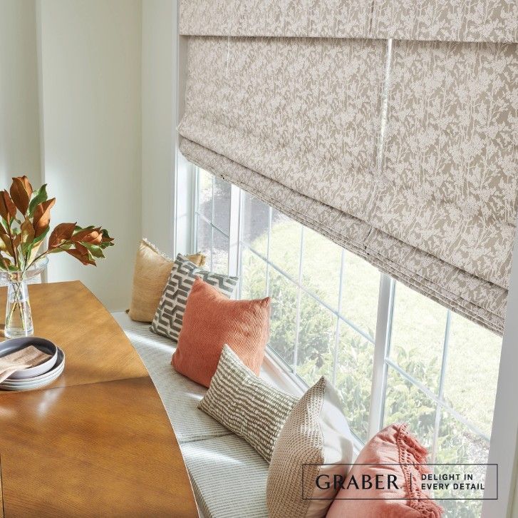 A living room with a window seat and a table with a vase of flowers on it.