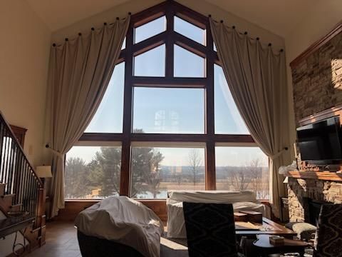 Sunlit living room with a tall arched window, beige curtains, stone fireplace, and cozy seating area