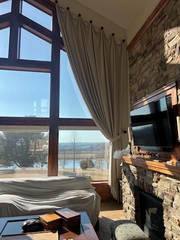 Sunlit living room with tall windows, stone fireplace, draped curtains, and a TV above the mantel