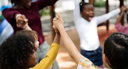 Children raising hands in a classroom, with one child in a yellow sweater in the foreground