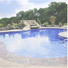 Pool with blue water and stone waterfall feature, surrounded by landscaping, under a partly cloudy sky.