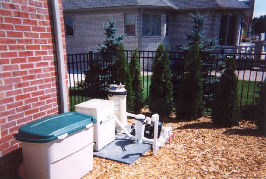 Pool equipment next to brick wall and landscaping, including filter, pump, and storage container.